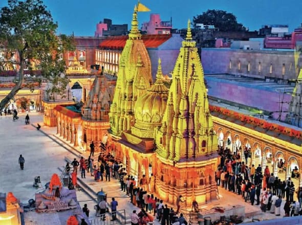 The golden spires of Shri Kashi Vishwanath Temple lit up at dusk, with devotees queuing in the courtyard